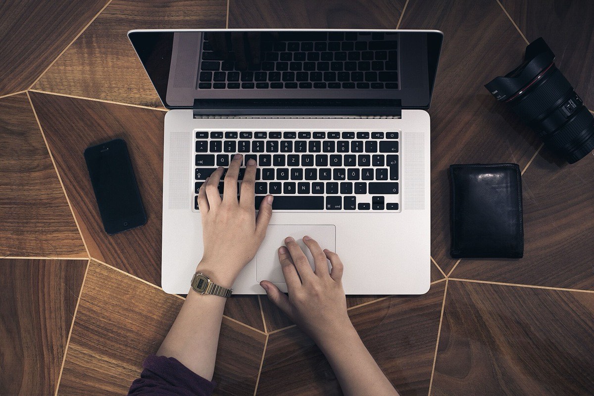 An overhead view of a desk, with a person's hands resting on a laptop keyboard.